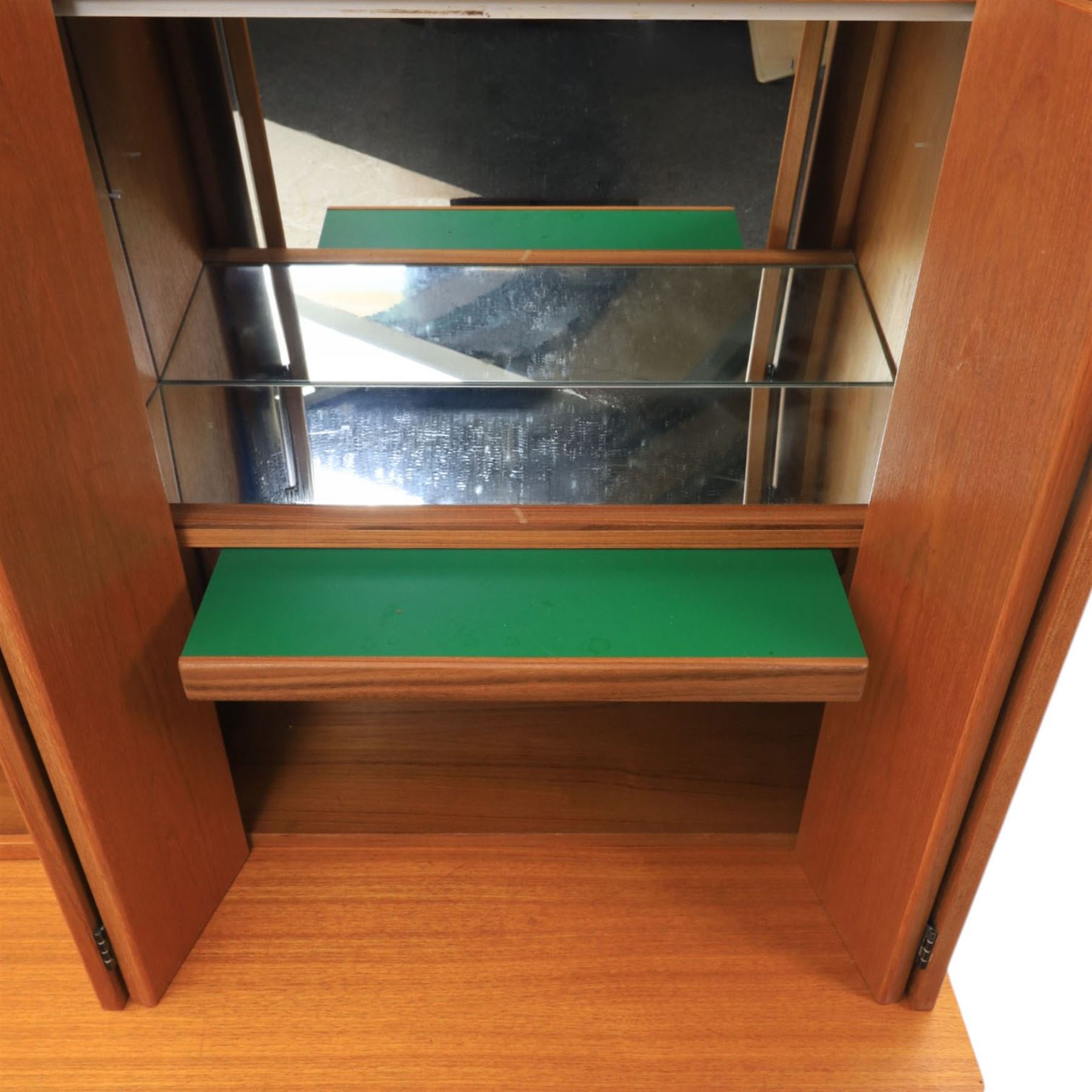 G-Plan - Mid 20th century teak modular wall unit, the upper section fitted with twin glazed doors enclosing shelves, adjoining concertina doors with mirrored and shelved interior, the base with four cupboard doors with recessed rectangular handles, raised on a plinth base