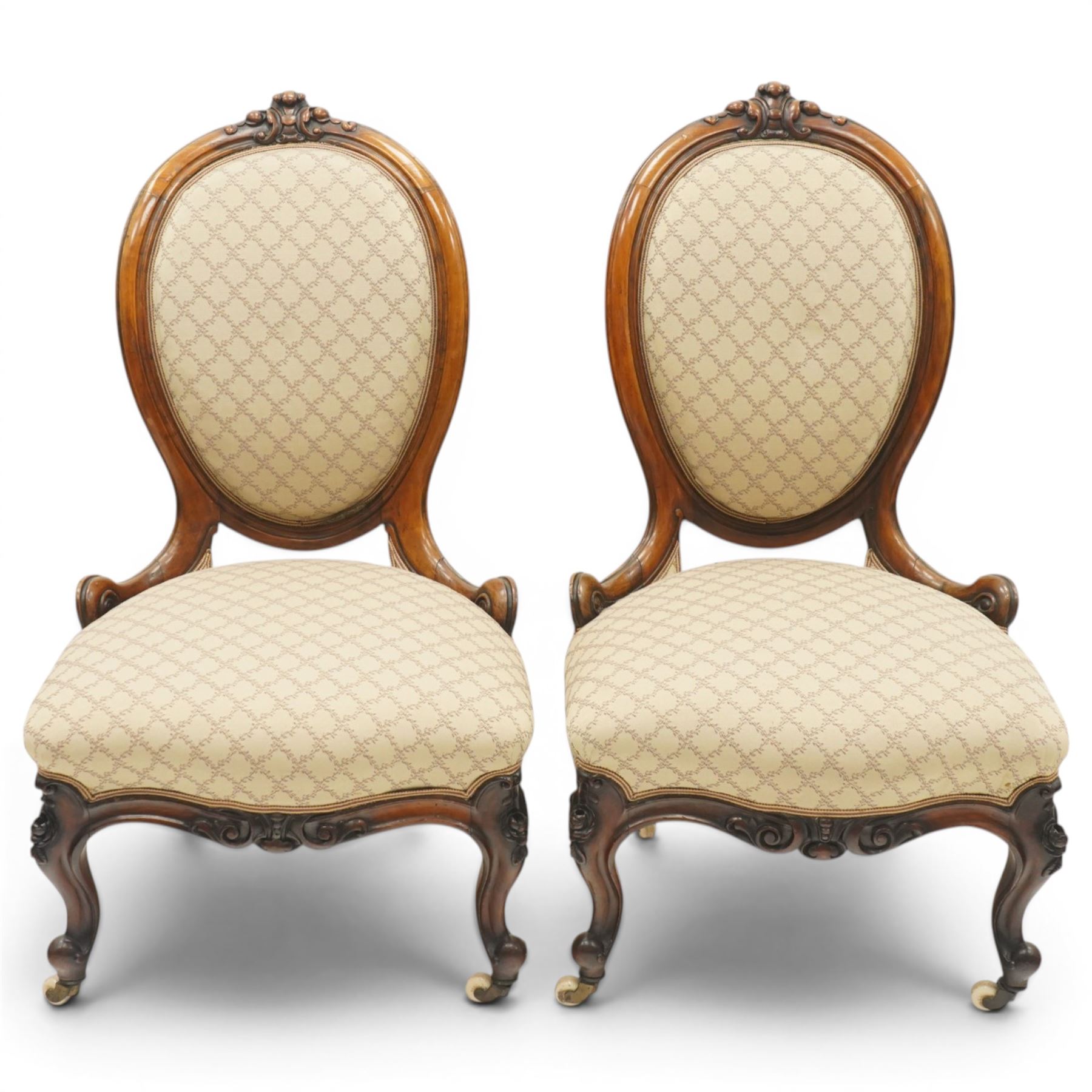 Pair of Victorian walnut framed ladies salon nursing chairs, oval cameo back with carved cartouche carved cresting rail, sprung seat upholstered in foliate patterned ivory fabric, shaped apron carved with scroll and cartouche decoration, on cabriole supports with moulded flower knees, retailed by David Hick Interiors, Jersey