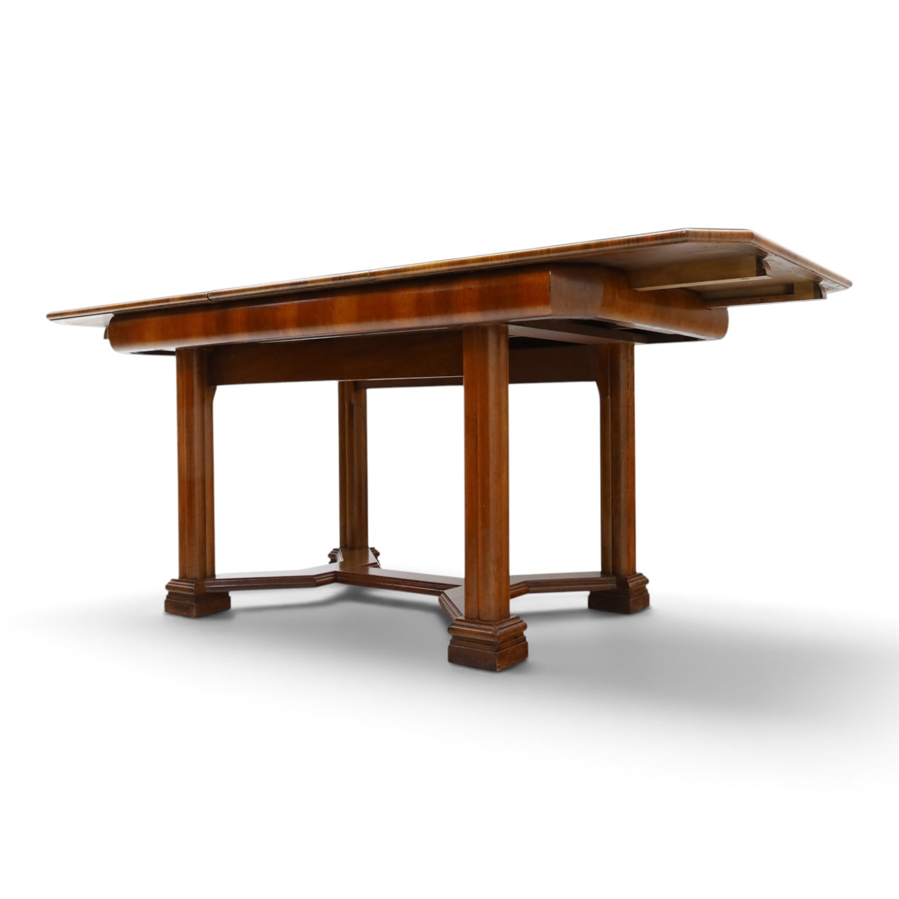 Art Deco walnut extending dining table, book-matched veneered shaped top, raised on cluster-column supports, united by stretchers, additional leaf extends to 185cm  