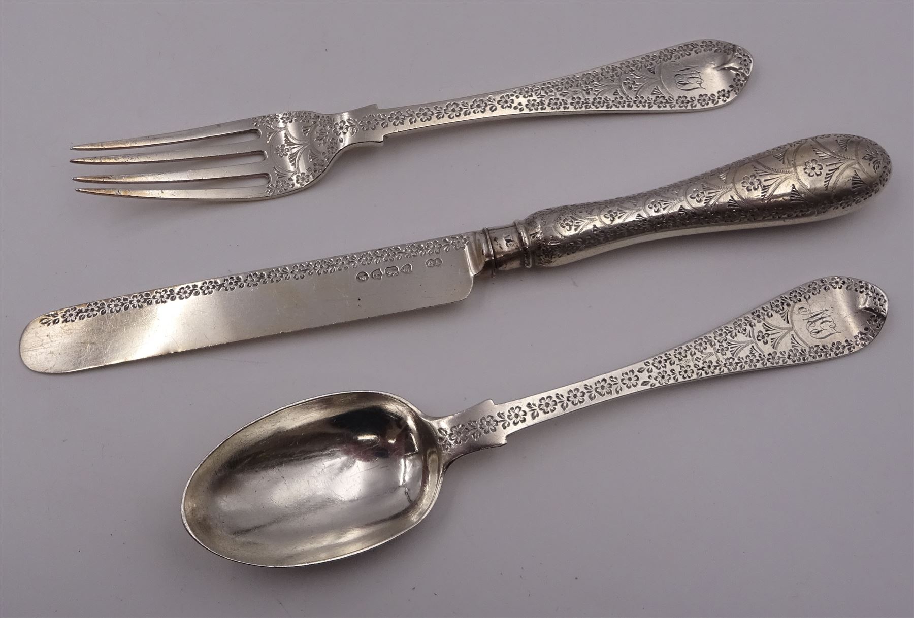 Victorian silver cutlery set, comprising knife, fork and spoon, all profusely engraved with flower heads, each with initials terminals, hallmarked Chawner & Co Birmingham 1877, contained within tooled leather, velvet and silk lined fitted case