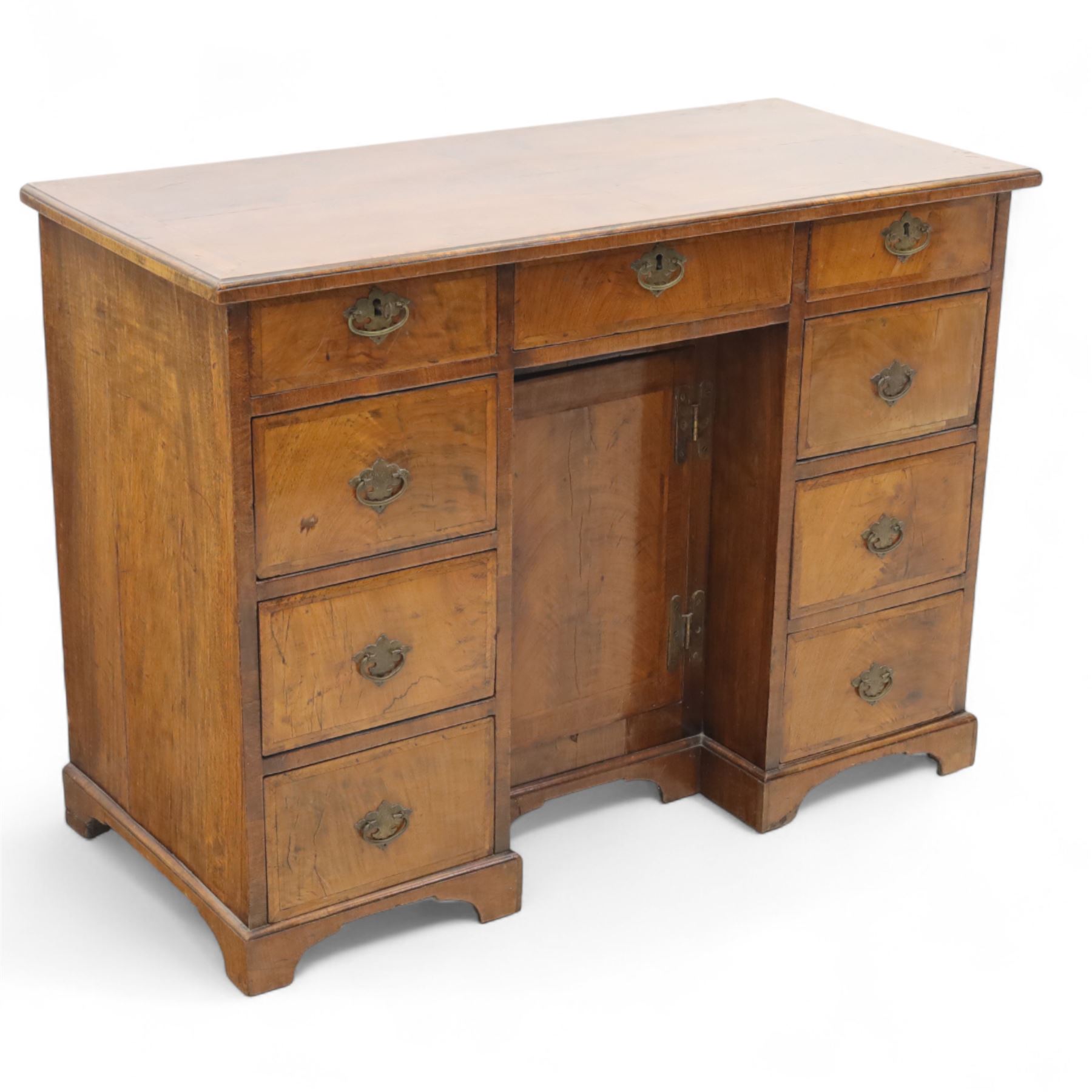 Early 20th-century Georgian-style walnut kneehole desk, the rectangular top with feather cross-banded border, above an arrangement of eight short drawers flanking a central cupboard door, fitted with brass backplate handles, raised on bracket feet