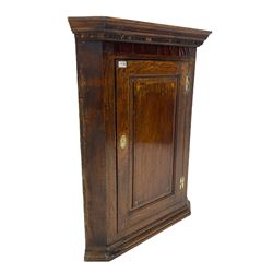 Georgian oak wall hanging corner cupboard, projecting dentil cornice over figured mahogany frieze and fielded panelled door, the interior fitted with three shaped shelves