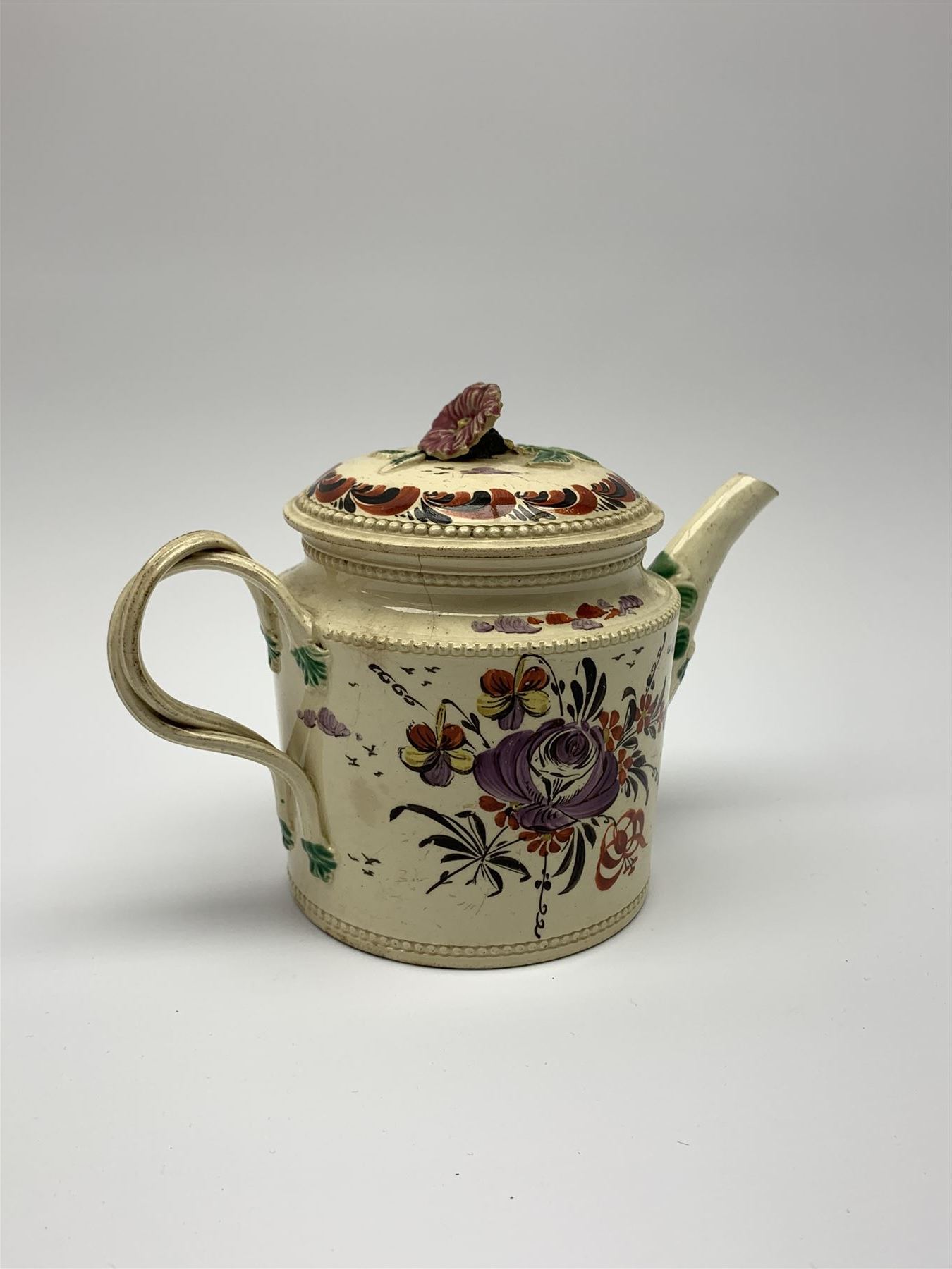 18th century creamware teapot, probably Leeds, with reeded entwined handle and floral finial to the cover, the body with hand painted polychrome decoration of figure to one side, and floral spray to the other, collectors paper label beneath inscribed Leeds Pottery, H11.5cm