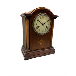 An early 20th century mantle clock in a mahogany case with a break arch pediment, supported by two circular wooden columns with brass capitals, satinwood stringing and inlay to the front, moulded plinth raised on four bun feet, with a white enamel dial, upright Arabic numerals and minute markers, steel spade hands enclosed in a convex glass with a brass bezel, eight-day HAC striking movement, striking the hours and half hours on a coiled gong, with countwheel striking and a recoil escapement.
With pendulum and Key. 
*The crossed arrows trademark displayed on the gong stand of this clock represents the Hamburg American Clock Company (HAC) formed in Germany in 1873 by  Paul Landenberger and Phillipp Lang, many of their clocks were exported to England and America during the late19th and early 20th century.
