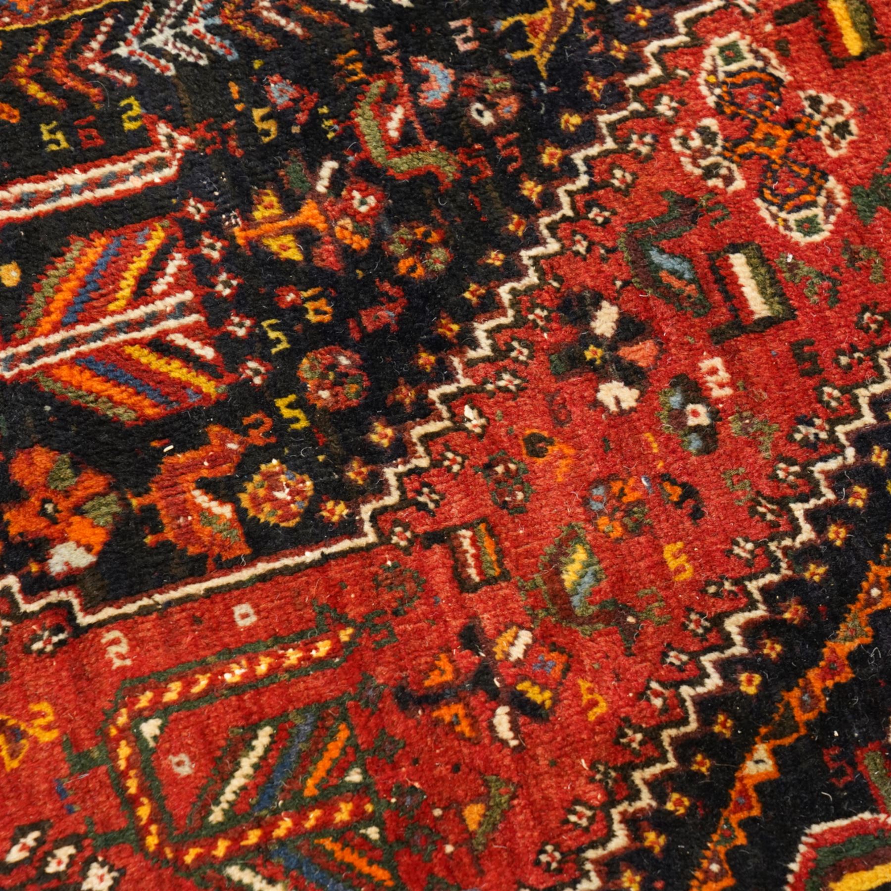 Persian Shiraz crimson ground rug, triple pole medallion surrounded by small stylised motifs depicting birds, animals and plants, within multiple band border each decorated with repeating patterns