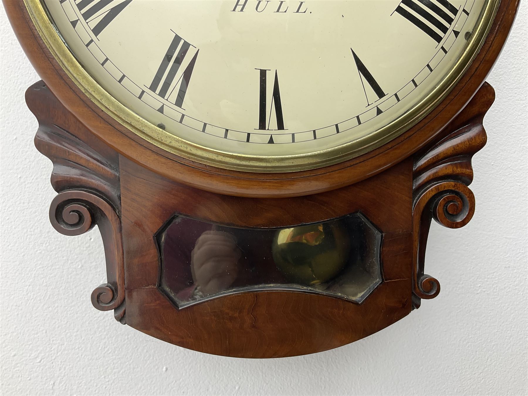A single fusee 8-day drop dial mahogany cased wall clock, c1860 with a 14-1/2” wooden bezel and 12” painted convex dial, cast brass bezel and convex glass, dial with retailer's name “Bedell & Son, Hull”, Roman numerals, minute track and matching steel moon hands, with a recoil anchor escapement and rectangular movement plates, case with scroll carved ears and glazed pendulum aperture, pendulum location door and a pendulum regulation door to the curved base. With pendulum.
***Peter and Benjamin Bedell were a family of 19th century Hull clockmakers working from various locations in Hull between 1823 and 1872.
