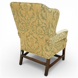 George III wing back armchair, the tall upholstered back with deep wings and gently shaped outline, padded arms flowing into the seat, loose cushion seat upholstered in a foliate patterned fabric, standing on square legs joined by stretchers