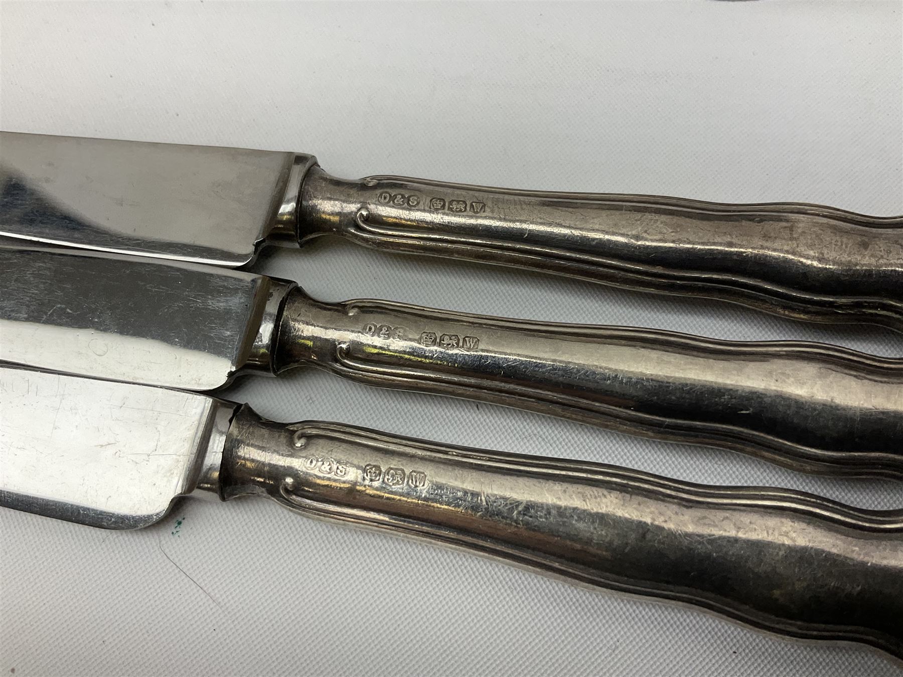 Two silver napkin rings, silver spoon with thistle top terminal, two silver handled butter knives, and small glass jar with silver cover, all hallmarked, approximate weighable silver 53.7 grams