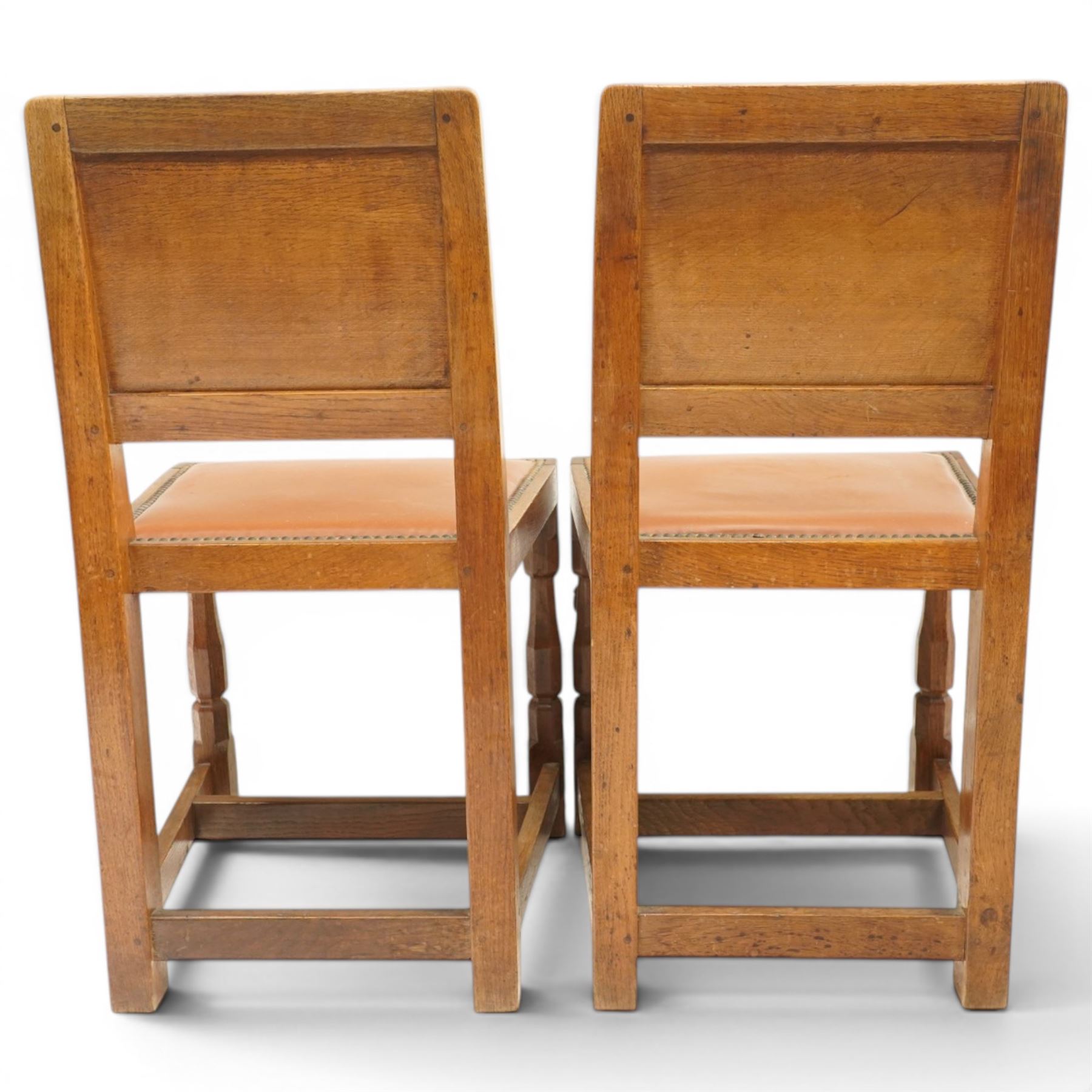Mouseman - pair of 1940's adzed and panelled oak chairs, the rectangular adzed back-panel over seats upholstered in orange-tan leather with studwork, raised on turned octagonal supports united by box stretcher, with carved mouse signature, by the workshop of Robert Thompson of Kilburn
Provenance: purchased directly from the Kilburn workshop in the late 1940s