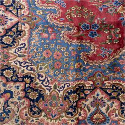 Large Central Persian Kirman hand-knotted carpet, raspberry red field, with central shaped medallion surrounded by an intricate arrangement of scrolling vines and floral sprays, within conforming spandrels and a pale blue border decorated with floral motifs, enclosed by guard stripes, with cotton fringe ends 