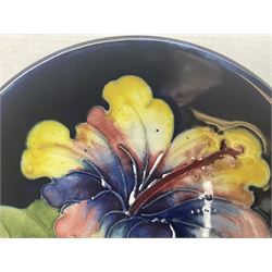 Moocroft small footed circular dish decorated in the Hibiscus pattern upon cobalt blue ground, with Queen Mary paper label beneath, together with a smaller example decorated in the Orchid pattern with impressed and printed W.Moorcroft marks beneath, largest, D9cm, (2)