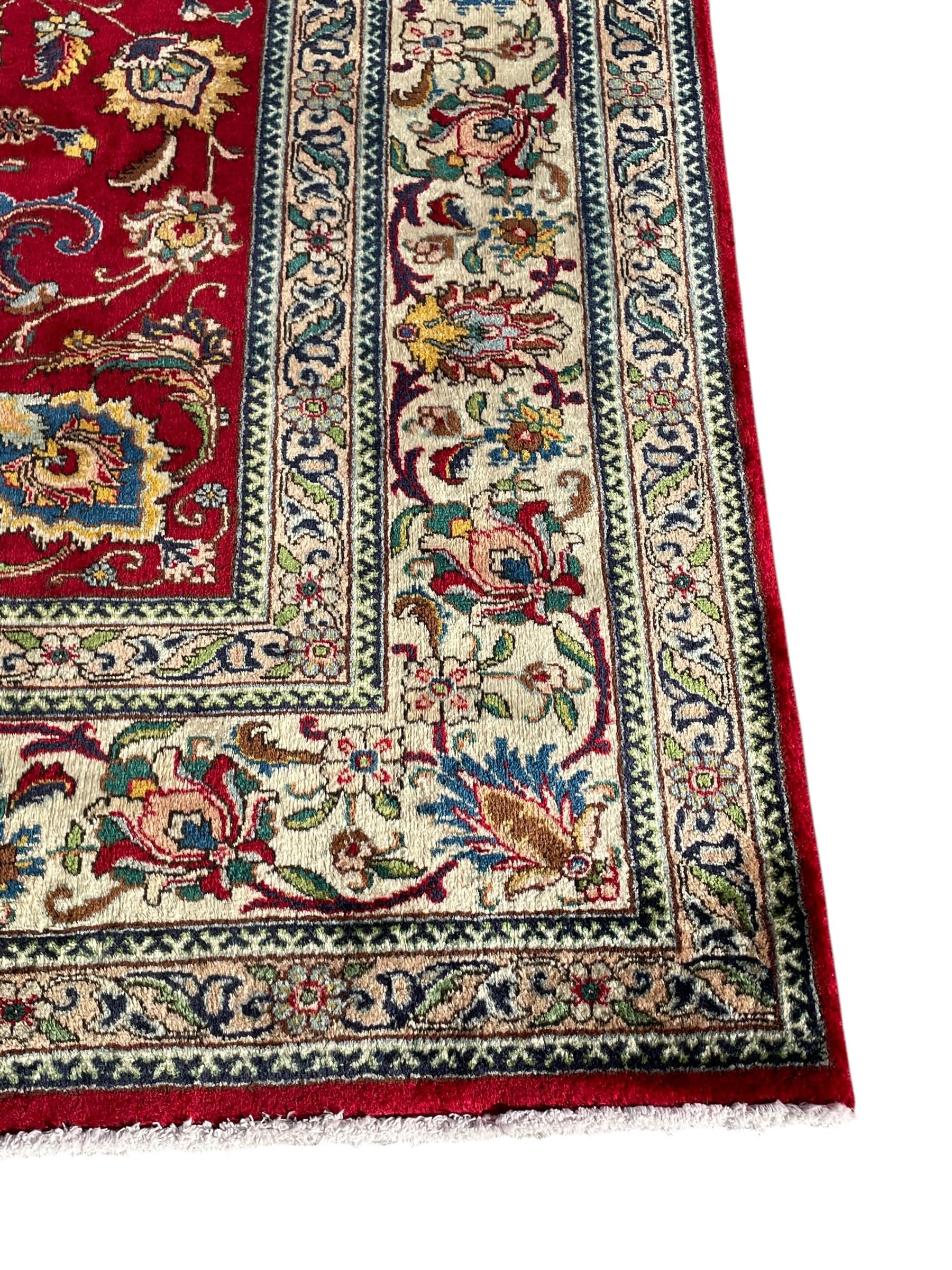 Persian Tabriz crimson ground carpet, decorated with swirling leafy branches and large palmette motifs, the pale ground border decorated with trailing foliate pattern, within floral guard stripes