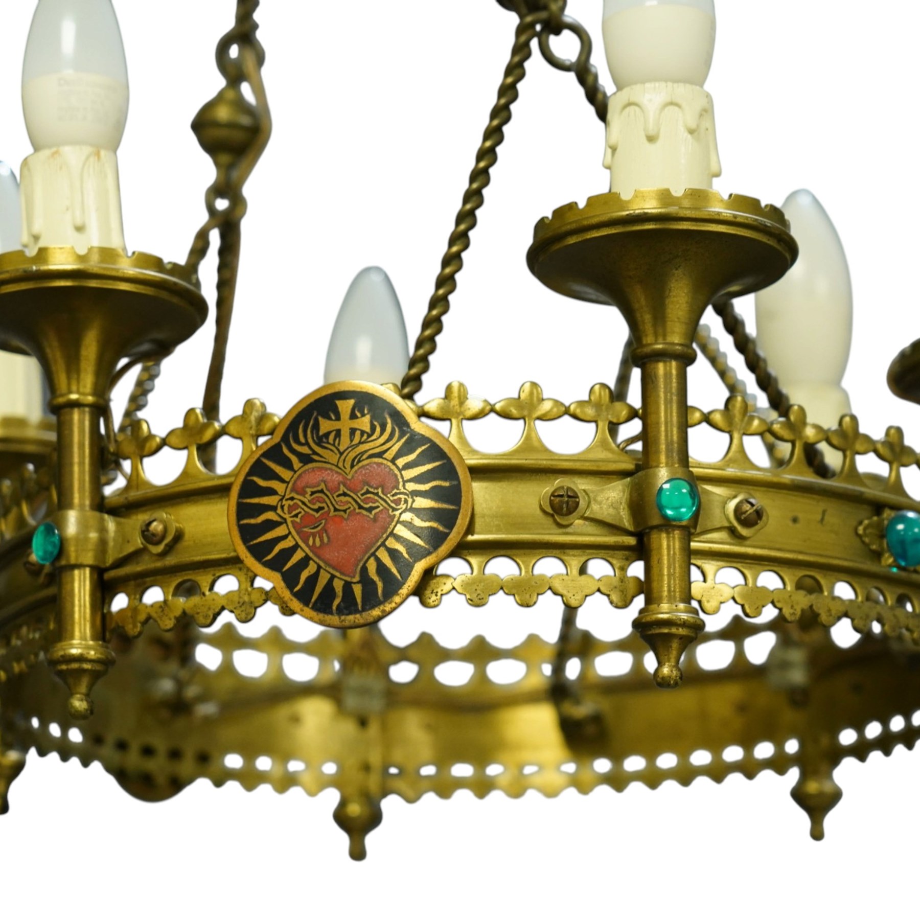 Gothic Revival brass six-light ecclesiastical chandelier, circular frame with pierced trefoil cresting and apron, applied with polychrome Sacred Heart medallions, six candle-form electric sconces, suspended on twisted brass rods and chains from a coronet-form ceiling boss