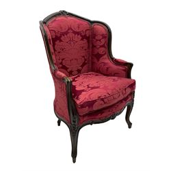 French style beech armchair, the moulded frame carved with flower heads and foliage, upholstered in red Damask fabric with floral pattern, shaped apron on scroll carved cabriole supports