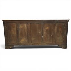 19th century Georgian oak long dresser base, rectangular plank top above a central frieze drawer over a fielded panel cupboard, flanked by three banks with quarter cantered pilasters, brass swan neck handles and escutcheons, raised on shaped bracket feet