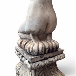 20th century composite stone garden figure, modelled as a kneeling nude female with arms raised behind her head, mounted on an integral cushion, the squared ogee pedestal moulded with acanthus leaves and flower heads, in a white painted and weathered finish