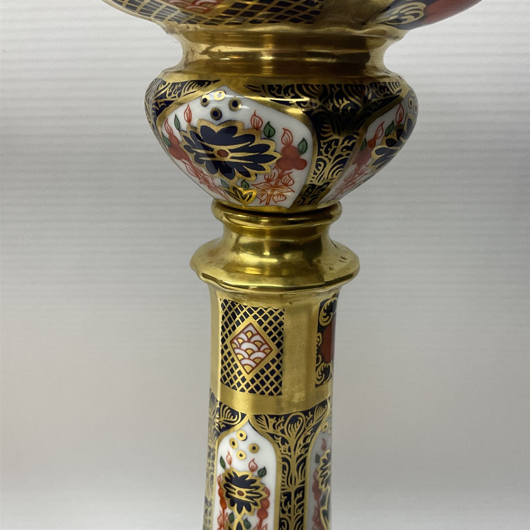 Pair of modern Royal Crown Derby Old Imari 1128 pattern candlesticks, each with shaped drip tray affixed to squat socket, upon spreading stem and canted square base with gilt dolphin edges, with printed marks beneath including Roman numeral year cypher for 2003, H26.5cm, with original boxes