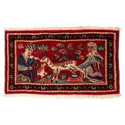 Two small rugs, an ivory ground example decorated with a central floral medallion and scattered rose sprays, enclosed by a navy foliate border (62cm x 101cm), and a crimson pictorial mat worked with seated figures, an animal and birds amongst flowering plants (45cm x 79cm) (2)