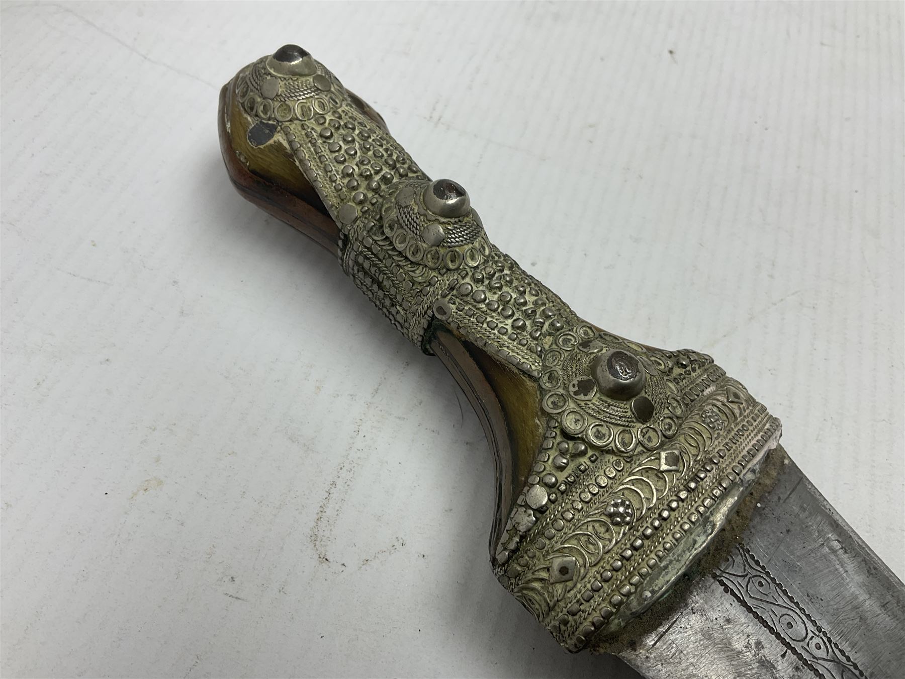 Saudi Arabian khanjar dagger with 29.5cm curving double edged  steel blade; white metal and copper mounted horn grip; in white metal mounted brass and leather scabbard incorporating embroidered leather wearing strap