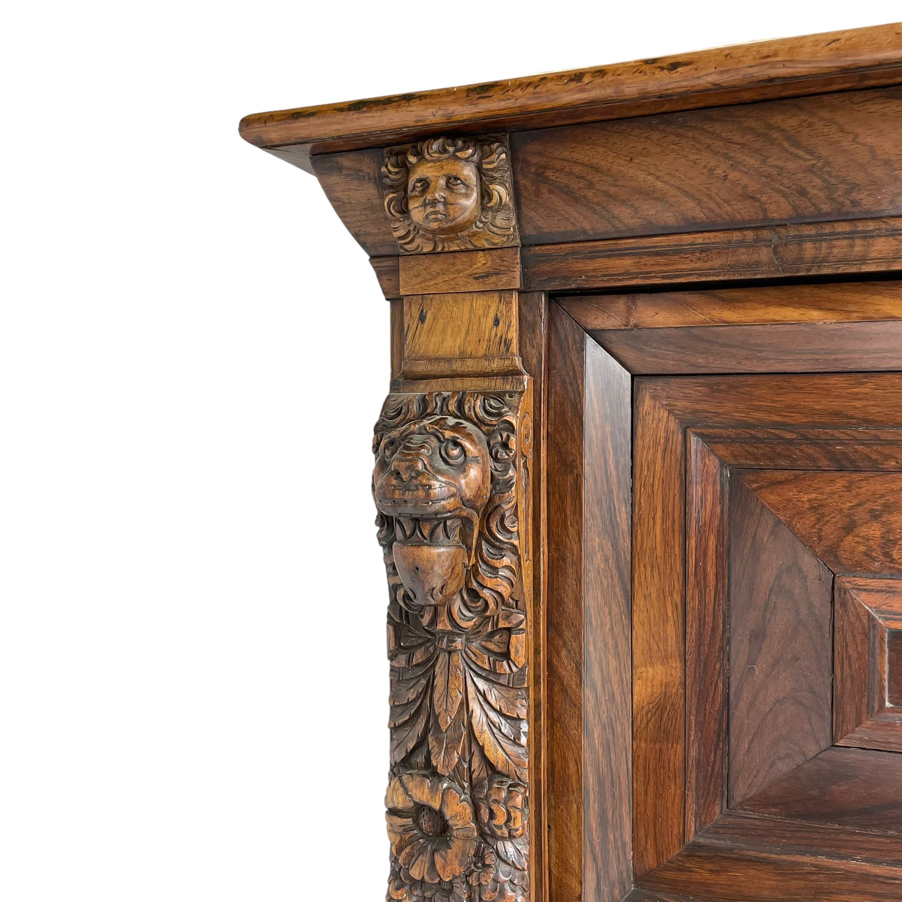 Late 17th century Flemish/Dutch rosewood and oak ‘Zeeuwse Kast’ or cupboard, projecting cornice carved with three putti masks, the uprights carved with lion masks over ribbons, flower heads and foliage, enclosed by four geometric panelled doors, lower central upright carved with flower head over foliate ribbon with bird among foliage, the escutcheon hidden by swivel berry carved cover, interior fitted with shelves, two drawers and shallow hinged cupboard, on two large turned and ebonised feet, circa 1680