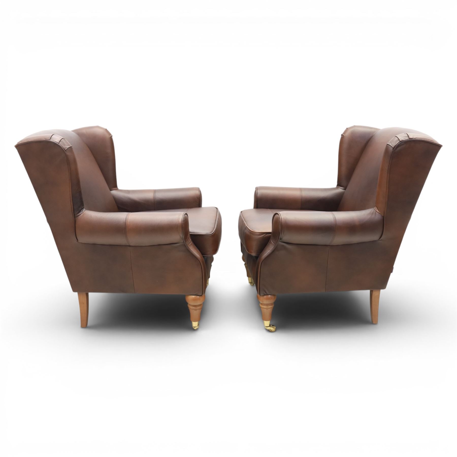 Marks & Spencer - Pair of brown leather wing back chairs, raised on light stained supports with castors