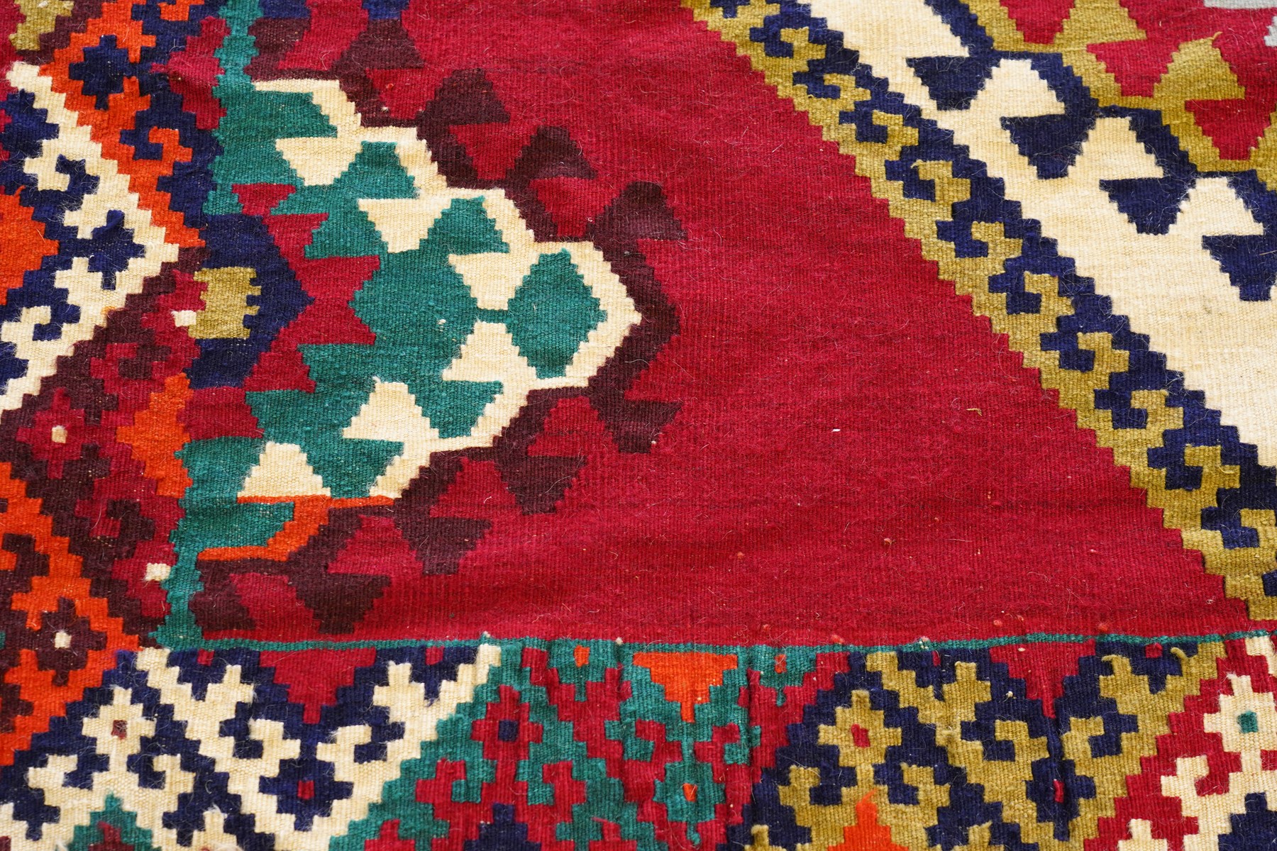 Persian Qashqai crimson ground rug, the central narrow ivory field decorated with repeating hooked geometric lozenges in multicolours, with a densely decorated guard band