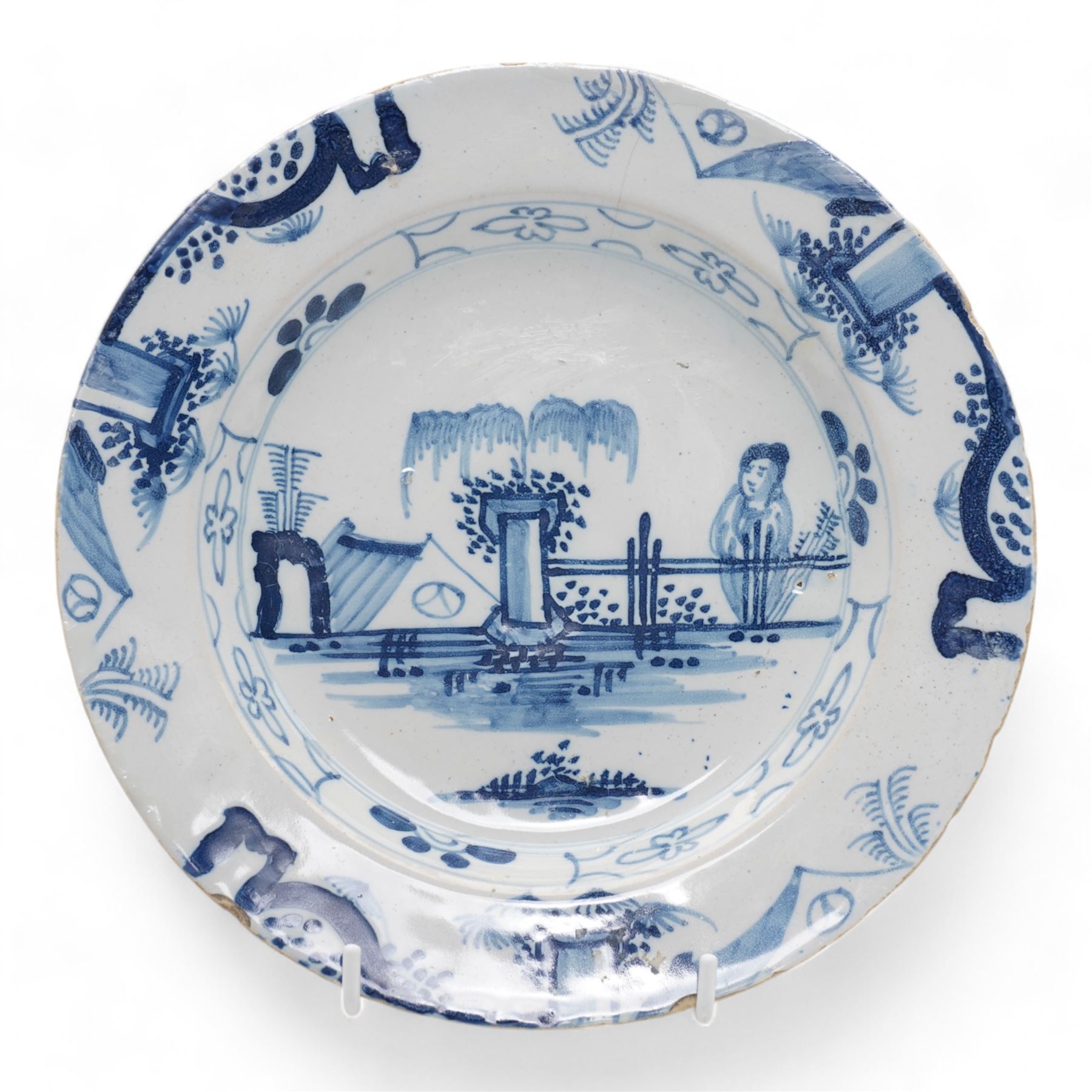 First Period Worcester plate, decorated in the Pine Cone pattern, cresent mark beneath D22.5cm, together with an 18th century Delft plate, painted with a Chinese figure by a fence, D23cm (2)