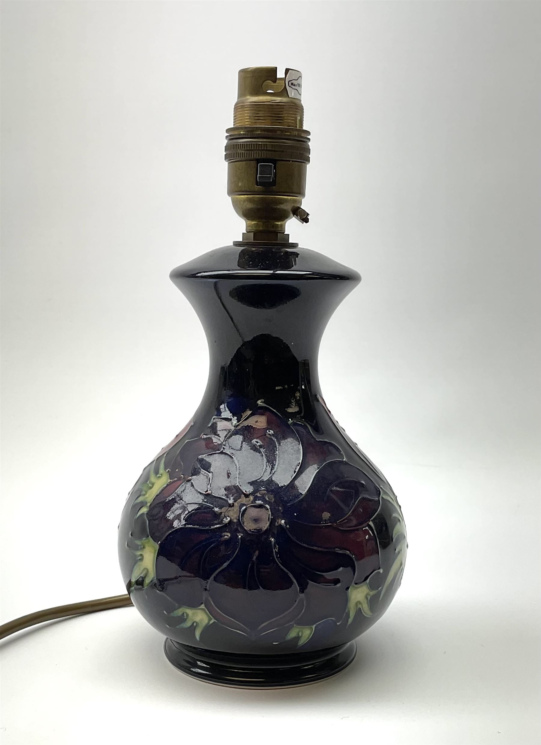 A Moorcroft table lamp, of baluster form, decorated in the Anemone pattern upon a dark blue ground, with impressed marks beneath, with accompanying cream shade with piped detail, overall H38.5cm.