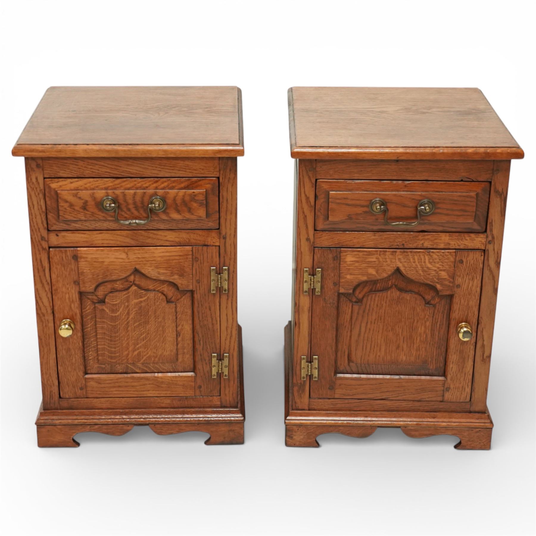 20th century pair of oak bed side cabinets, in the manner of Titchmarsh & Goodwin, plain rectangular tops over drawers fitted with brass handles and cupboard doors with carved arched panels, panelled sides and backs, raised on shaped bracket feet