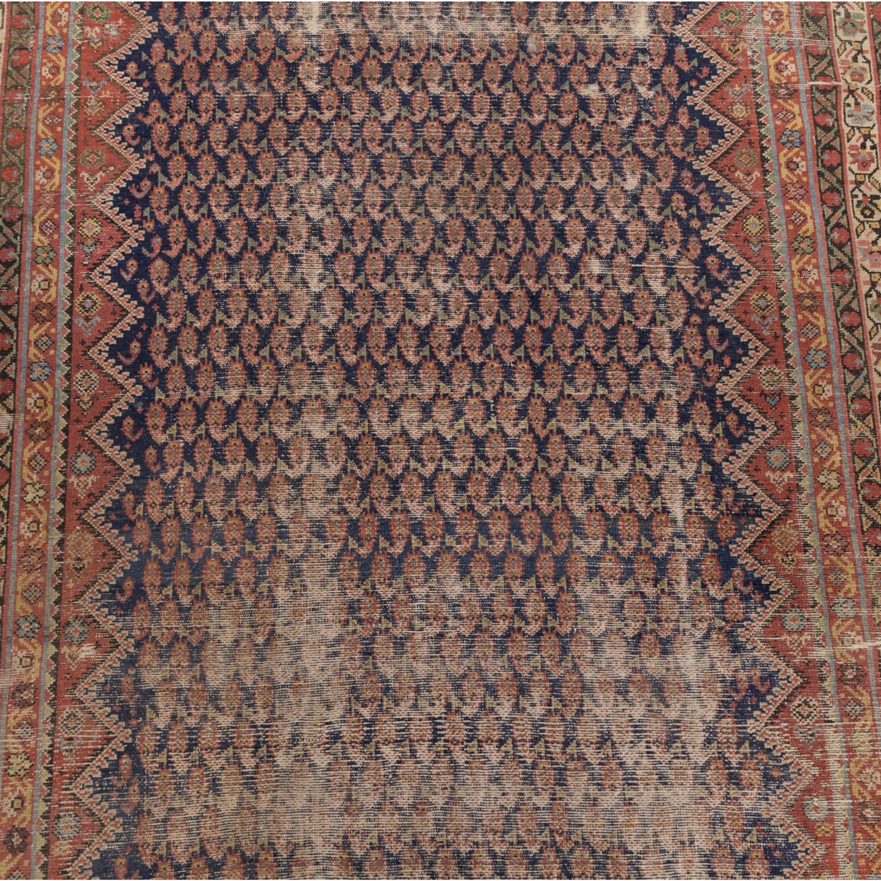 West Persian Kurdish vintage carpet, indigo field decorated with an all-over repeating boteh design arranged in diagonal rows framed by angular spandrels and enclosed by multiple geometric borders in a palette of indigo blue, madder red, soft green and ivory