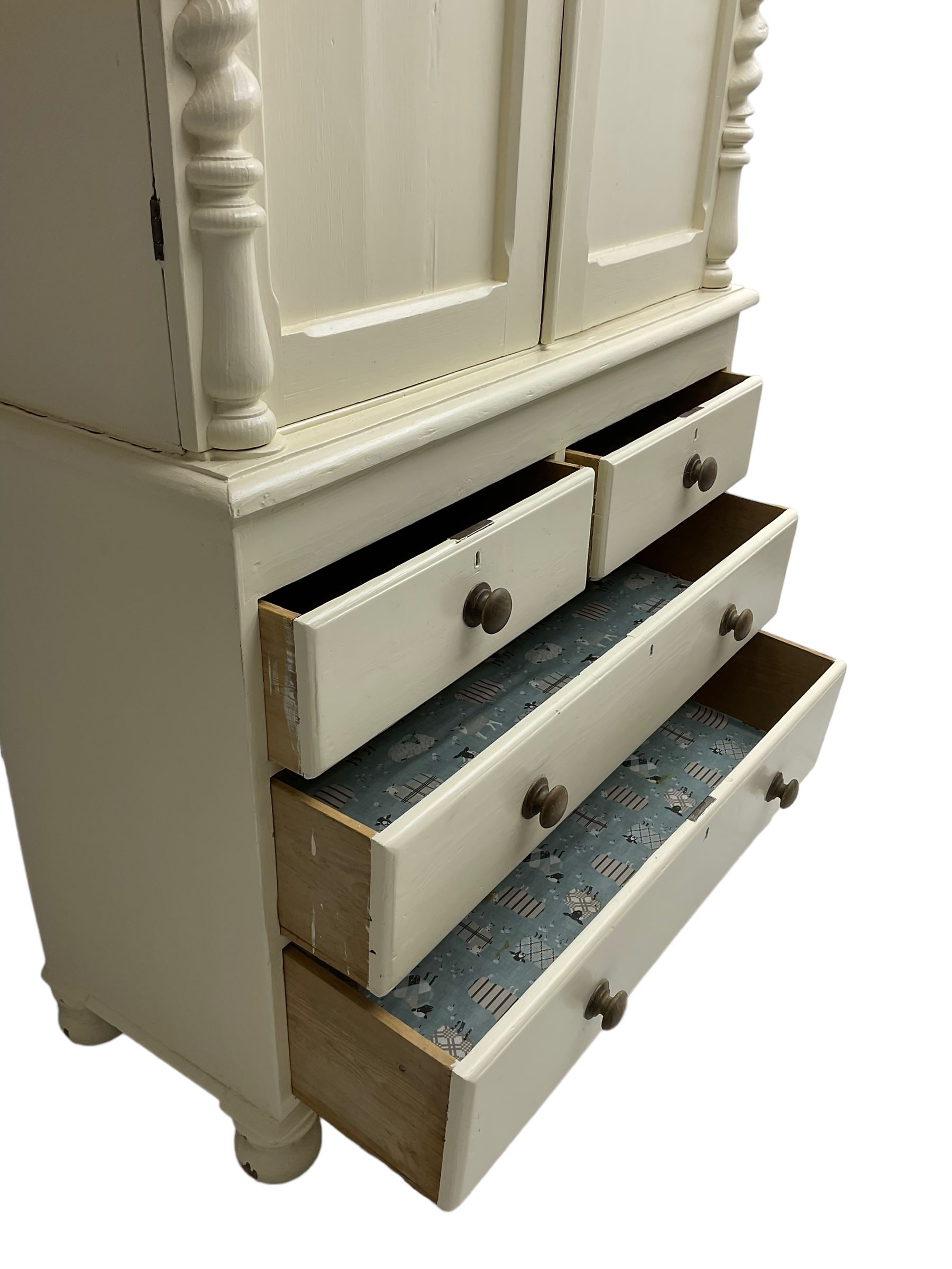 Victorian cream painted pine cupboard-on-chest or housekeeper's cupboard, projecting cornice over two double-arch panelled cupboard doors enclosing two shelves, flanked by spiral turned uprights, base fitted with two short over two long drawers, on bun feet
