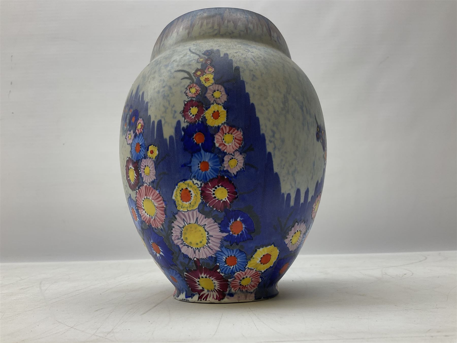 1930s Carlton Ware Art Deco Garden pattern vase of shouldered ovoid form, decorated with blue, pink and yellow flower heads on a mottled blue and white ground, pattern no. 3413, with printed and painted marks beneath, H19cm, together with a Clarice Cliff My Garden pattern vase, raised upon three feet with blue, pink and purple moulded Hollyhock design, H20cm, with Clarice Cliff Wilkinson Ltd England marks beneath