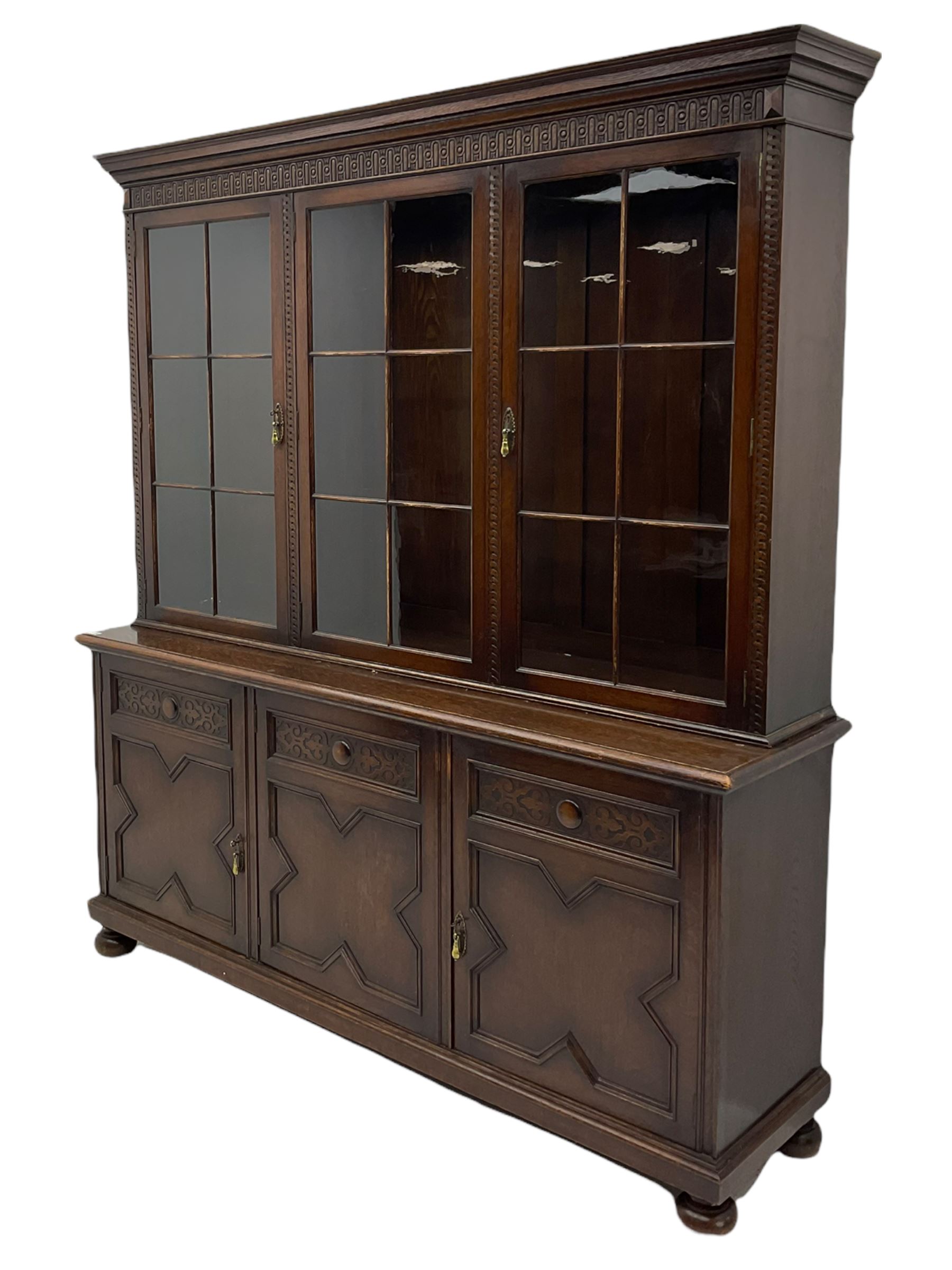 Waring and Gillow - oak bookcase on cupboard, projecting cornice over arcade frieze, guilloche upright decoration, the top section enclosed by three astragal glazed doors, the lower section enclosed by three geometric panelled doors with blind fretwork decoration, on turned feet