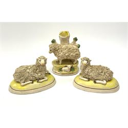 A 'Staffordshire' garniture modelled as sheep, comprising central spill vase with sheep and lamb, and two Victorian flanking recumbent sheep, each sheep with textured fleece body, upon a yellow and gilt detailed base, central example H13cm. 
