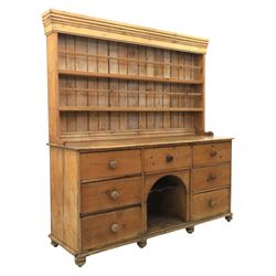 Early 19th century waxed pine farmhouse dresser and rack, the rack featuring two plate shelves and bars above seven drawer base with centre 'dog kennel' recess, raised on turned feet