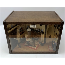 A 1/12th scale diorama of a cottage sitting room, depicting an elderly lady seated before a fireplace knitting, with dog and cat, in an interior furnished with blue and white plates, Staffordshire figures, toby jug, brass horse shoes, copper kettle, etc., H29cm L40cm D26cm.