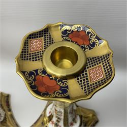 Pair of modern Royal Crown Derby Old Imari 1128 pattern candlesticks, each with shaped drip tray affixed to squat socket, upon spreading stem and canted square base with gilt dolphin edges, with printed marks beneath including Roman numeral year cypher for 2003, H26.5cm, with original boxes