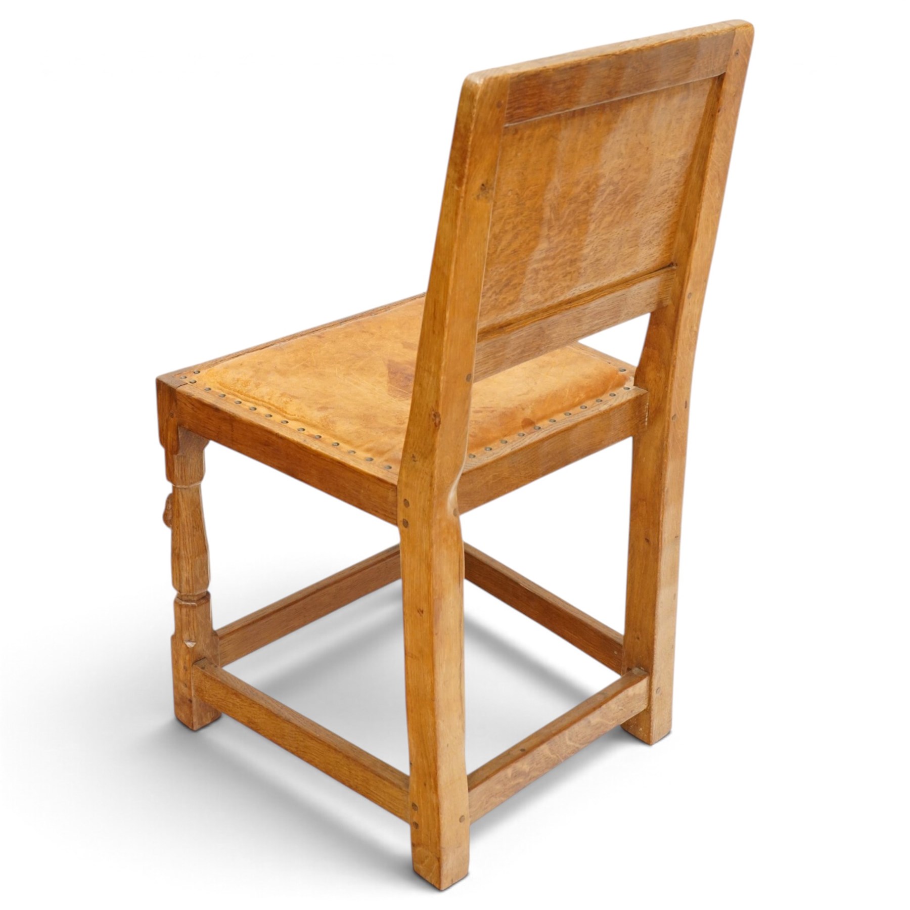 Mouseman - set of six (5+1) 1940s pre-war panel-back dining chairs, the raised backs with adzed panels, over seats upholstered in tan leather with studwork border, raised on octagonal turned baluster supports united by box stretcher, with carved mouse signature, by the workshop of Robert Thompson of Kilburn

Provenance: ordered directly from the Mouseman workshop in the 1940s before the outbreak of the war, the items were subsequently delivered after the end of war. 