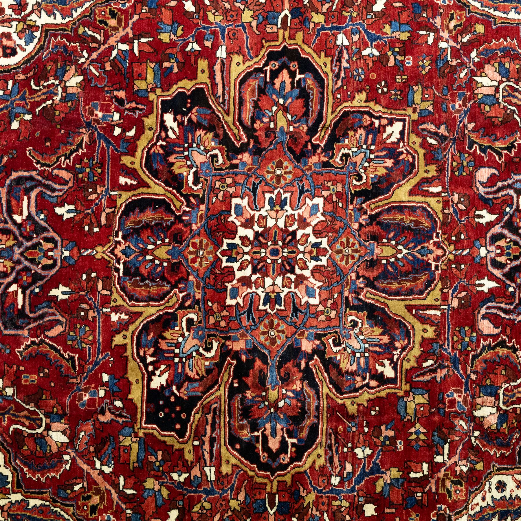 North West Persian Ahar hand-knotted carpet, madder red ground, with a large central shaped floral medallion with pendants, surrounded by angular scrolling foliate motifs incorporating rosettes, palmettes and stylised flowerheads, enclosed by ivory spandrels and a dark navy border with repeating geometric floral motifs and meandering vines, flanked by narrow patterned guard stripes, with cotton fringes