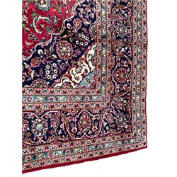 Central Persian Kashan crimson ground carpet, central  floral pole medallion with matching spandrels within a field of scrolling palmette motifs and foliage, the heavily banded indigo border with repeating plant motifs interlaced with scrolled branches