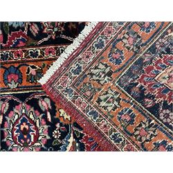 Persian Meshed carpet, plum ground and decorated with stylised flower heads and interlacing foliate, large central stylised medallion with orange detail, the orange mirrored in the five band border decorated with scrolling floral design, signature panel to end 