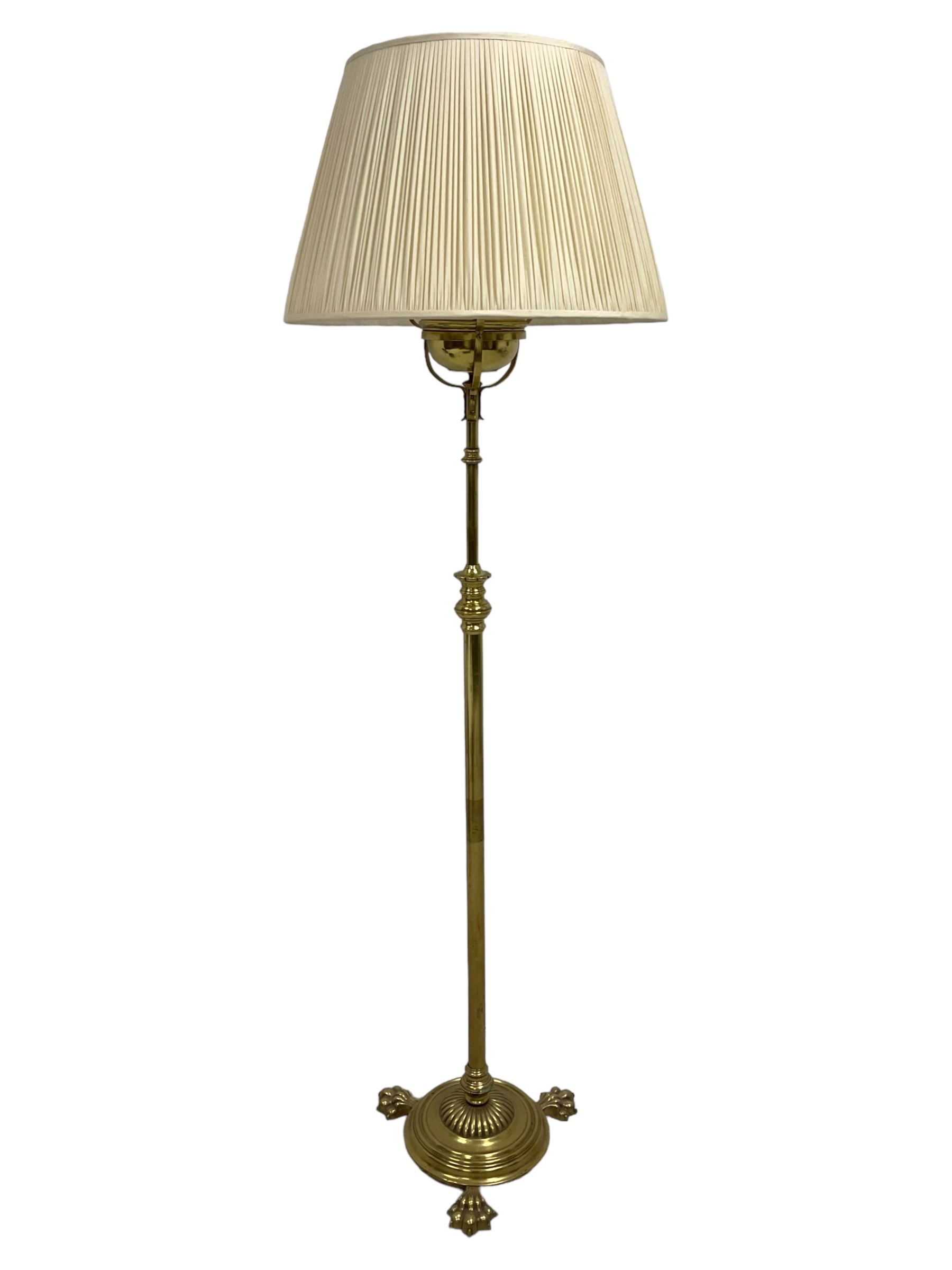 Edwardian brass plated copper standard lamp, telescopic stem on lobe moulded circular base with three projecting paw feet, with cream shade