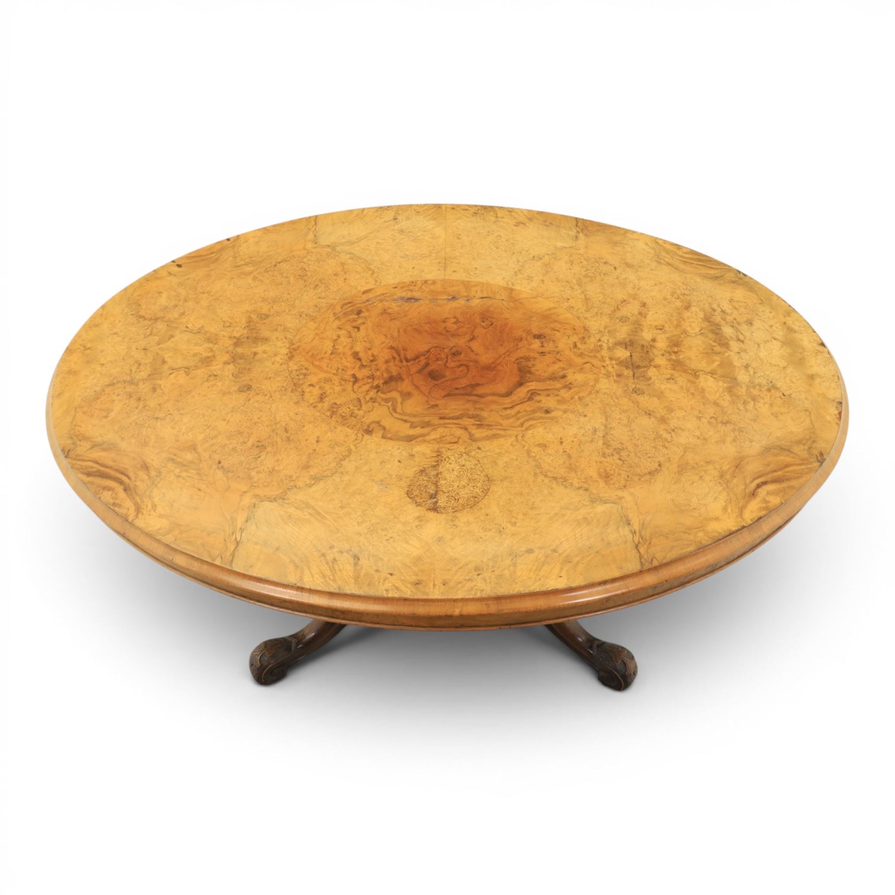 Victorian figured walnut oval loo tilt top table, raised on a heavily carved quatriform base with scrolled supports, terminating in castors