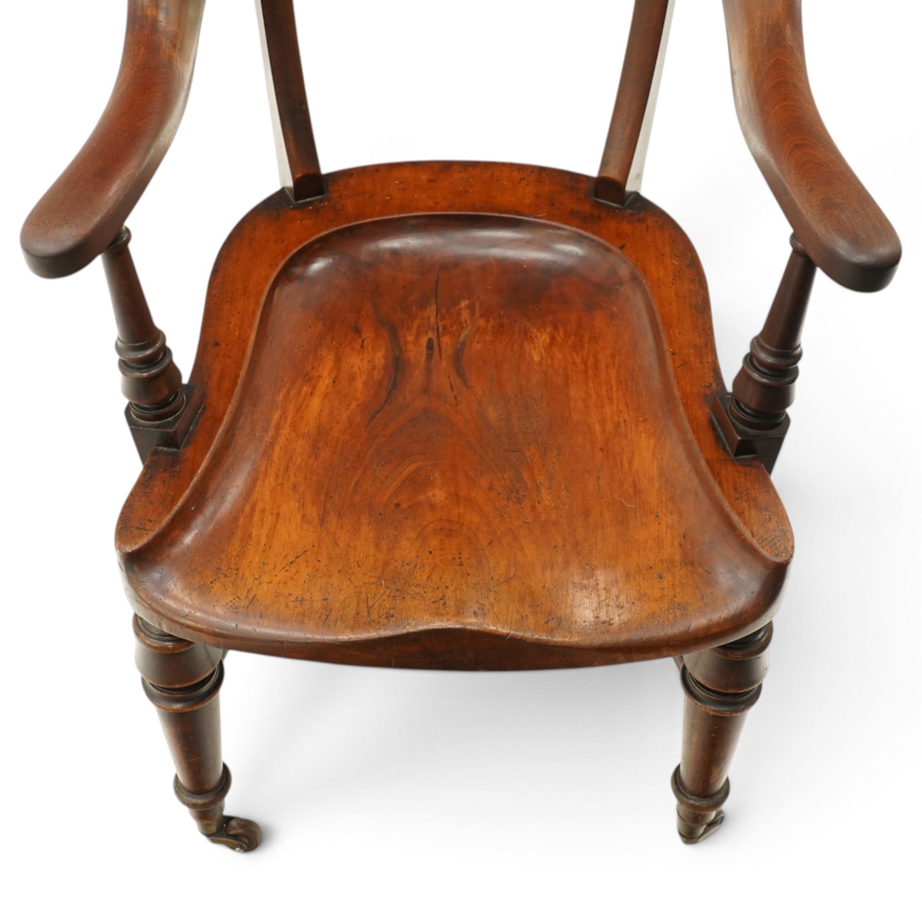 19th century carved mahogany Captain's desk chair, the bow-shaped cresting rail over curved back and turned arm supports, shaped saddle seat raised on turned supports united by crinoline stretcher, with brass cups and ceramic castors