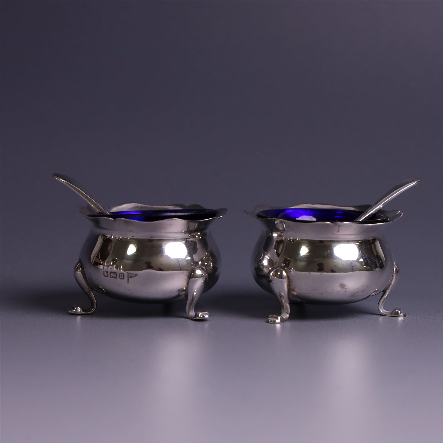 Early 20th Century four piece silver cruet set, comprising a pair of pepper shakers and a pair of open salts, each of circular form with shaped rims and upon three pad feet, hallmarked Walker & Hall, Sheffield 1912, the open salts with two silver plated salt spoons and blue glass liners 