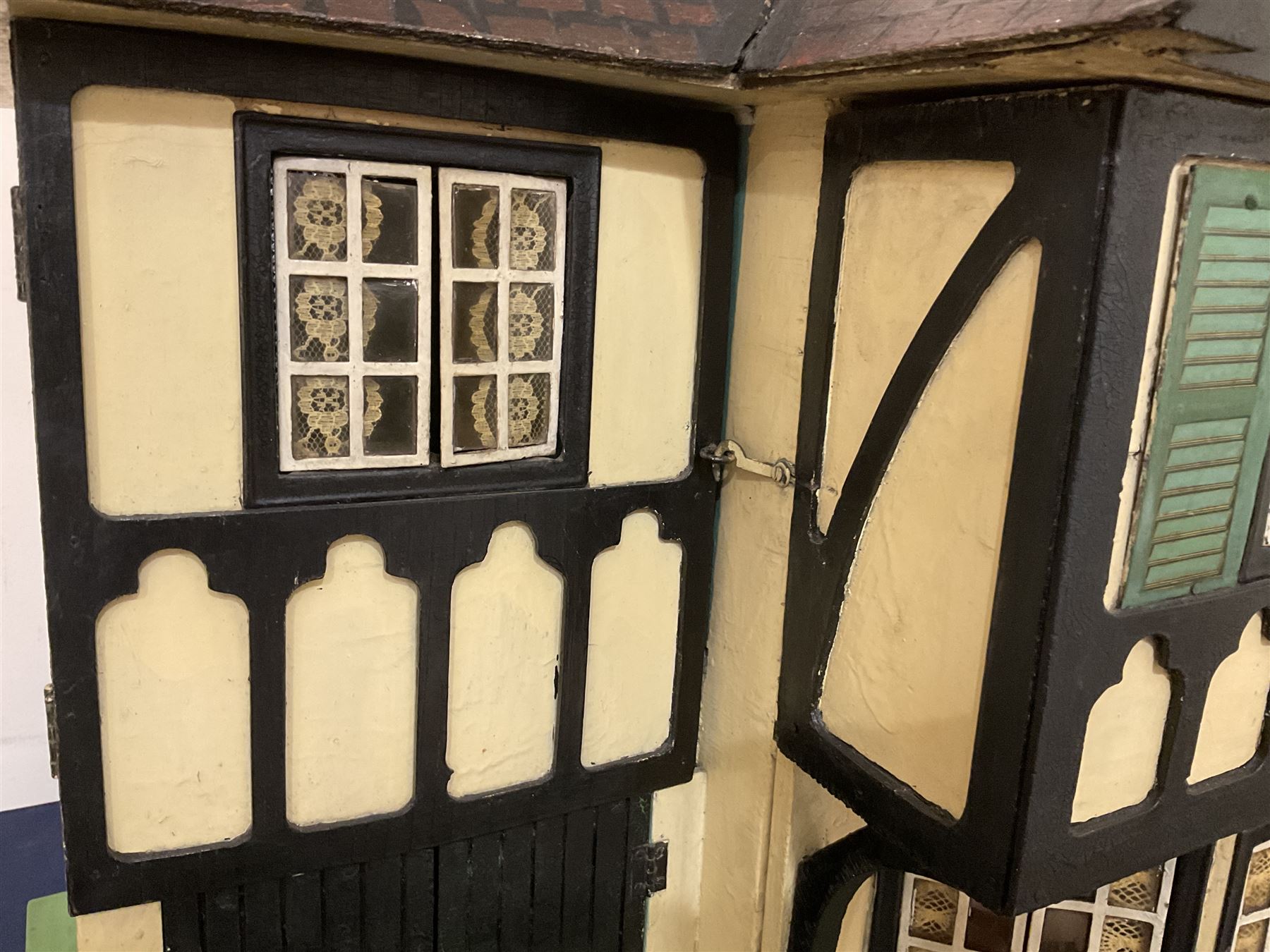 Large Tri-ang No.93 doll`s house in the 'Stockbroker's Range' c1935; two-storey double-fronted Tudor design, half timbered gables, two-storey bay windows, cream and mock shrubbery to front, opening metal framed windows with green shutters, red simulated tiled roof with chimney, integral garage with opening doors, front elevation has four hinged doors opening to reveal two bedrooms with fire places, living room, bathroom and kitchen with built in dresser and sink, entrance hall and staircase, side entrance with porch and seat and sun dial over on chimney stack; some wiring for electrical lighting; metal Tri-ang Toys disc verso; comprehensively furnished H66cm L117cm D43cm