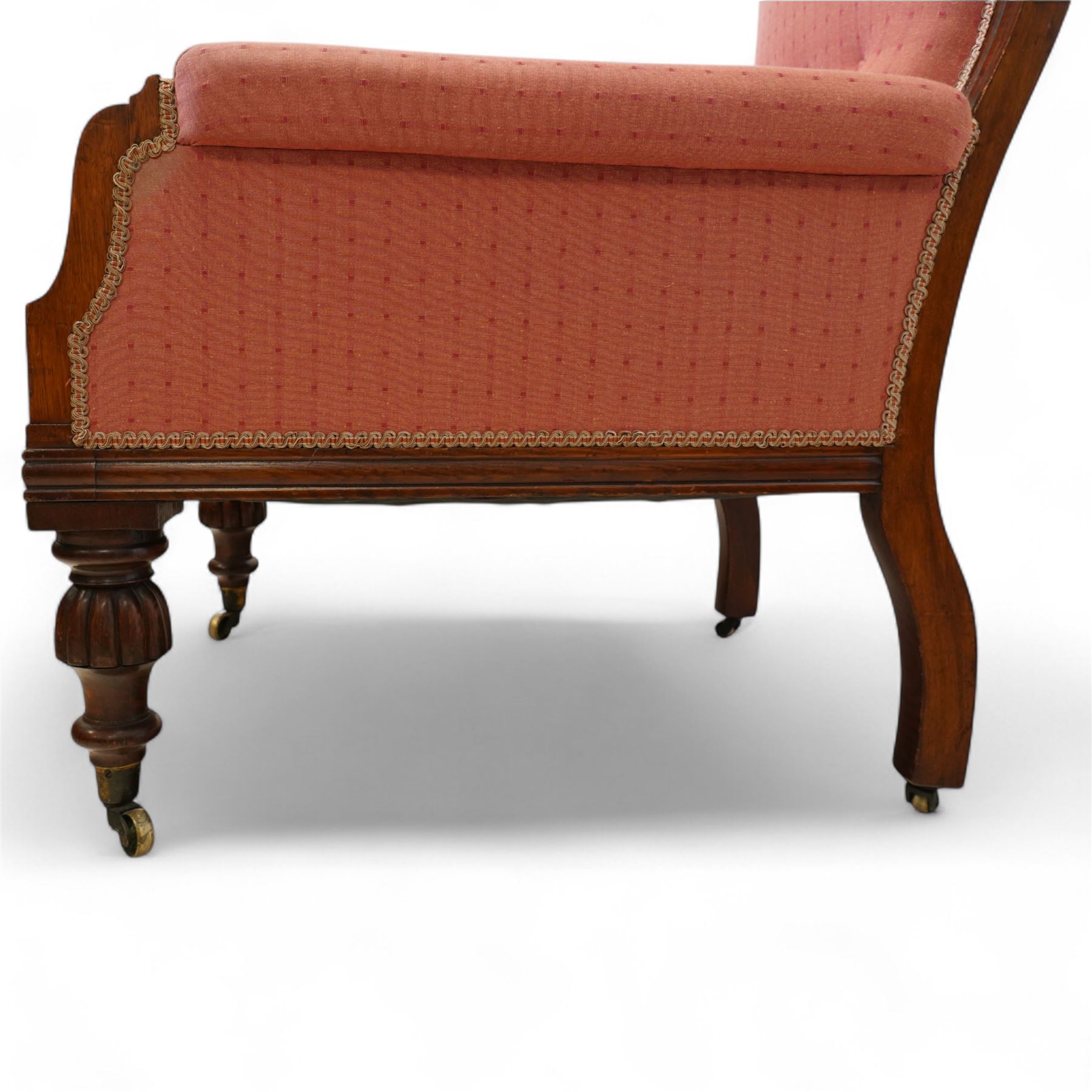 Victorian mahogany framed armchair, upholstered in salmon pink dot patterned fabric, the moulded arms with carved scroll terminals, raised on turned and fluted front legs and swept back legs, all with castors