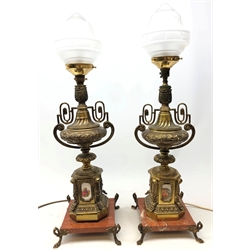  Pair French gilt metal and ceramic table lamps, each of two-handled urn form with ceramic printed panels depicting romantic scenes, raised on red veined marble plinths with scroll feet and frosted glass shades, H72cm   