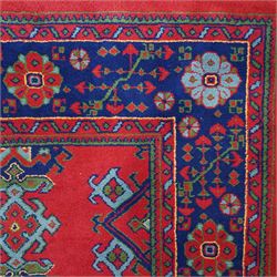 Indian Kayam rug, the rectangular field with repeating geometric medallions on a red ground, within a blue border of stylised floral motifs, with guard borders and fringe terminals
