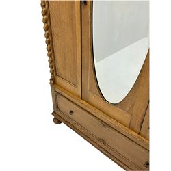 Early 20th century oak wardrobe, projecting cornice of blind fret-work frieze, oval bevel edge mirror door, half spiral turned pilasters, drawer to base with mouldings, on turned bun feet